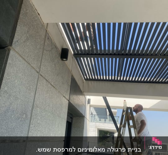 אדם על סולם מתקין פרגולת אלומיניום